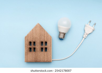 Energy Efficient Home Concept, Wooden House Model with LED Light Bulb and Electrical Plug on Blue Background - Powered by Shutterstock