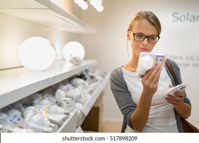 Energy Efficient Lighting Choice: Pretty, Young Woman Holding And Choosing A LED Diode Light Bulb For Her Lamp In DIY Department Store