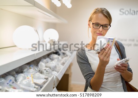 Energy efficient lighting choice: Pretty, young woman holding and choosing a LED diode light bulb for her lamp in DIY department store