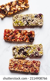 Energy granola bars with different seeds, nuts and dried fruits and berries on a white marble background, top view. Healthy snack concept.