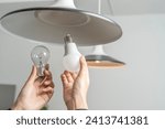 Energy saving idea: Asian people replace fluorescent light bulbs (CFL) with new LED bulbs. Female hands screw in an energy-saving LED light bulb.