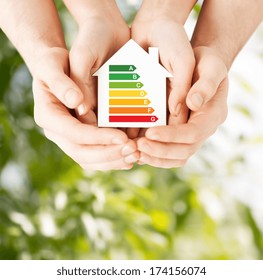 Energy Saving, Real Estate And Family Home Concept - Closeup Of Couple Hands Holding White Paper House With Energy Efficiency Rating