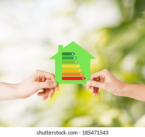 Energy Saving, Real Estate And Family Home Concept - Closeup Of Couple Hands Holding Green Paper House With Energy Efficiency Rating