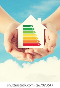 Energy Saving, Real Estate And Family Home Concept - Closeup Of Female Hands Holding White Paper House With Energy Efficiency Rating