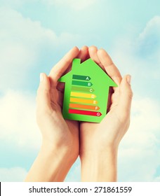 Energy Saving, Real Estate And Family Home Concept - Closeup Of Female Hands Holding Green Paper House With Energy Efficiency Rating