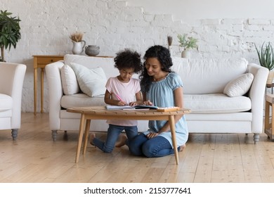 Engaged African American mom   daughter kid doing primary school homework together  writing  drawing in learning textbook  playing educational games in home interior  Full length shot