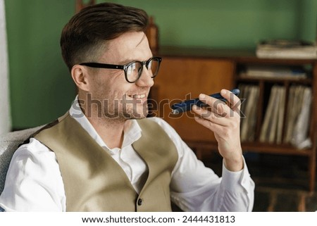 Engaged in a conversation, a man in a tailored vest uses his phone, surrounded by the warmth of his tasteful home office, hinting at a lifestyle that combines work and comfort.