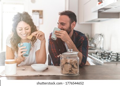 Engaged couple has breakfast together in their new home - young couple smiling while drinking and eating in the kitchen - warm filter on background - Shutterstock ID 1776544652