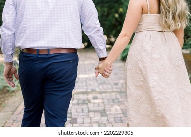 An Engaged Couple Holding Hands And Walking Away