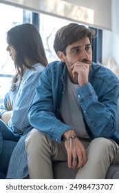 Engaged couple with relationship problems sitting on the sofa with their backs to each other after an argument, conflicts in marriage, upset couple after a dispute, making decision to break up divorce