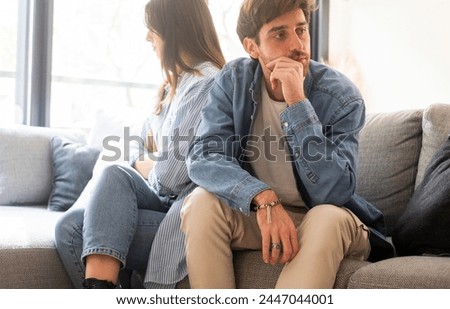 Engaged couple with relationship problems sitting on the sofa with their backs to each other after an argument, conflicts in marriage, upset couple after a dispute, making decision to break up divorce
