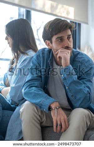 Engaged couple with relationship problems sitting on the sofa with their backs to each other after an argument, conflicts in marriage, upset couple after a dispute, making decision to break up divorce