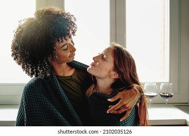 Engaged couple of young lesbian women holding together against the kitchen window drinking red wine - Powered by Shutterstock