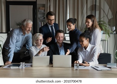 Engaged Diverse Business Team Looking, Pointing At Laptop Screen, Talking At Shared Workplace, Brainstorming, Working On Project Together. Mentor And Interns Discussing Content On Laptop