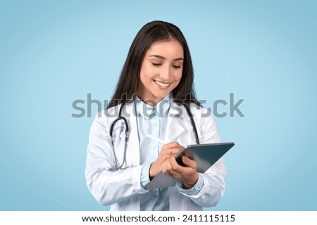 Engaged female doctor inputting data on tablet, exemplifying modern healthcare technology in practice, with pleased expression, blue backdrop