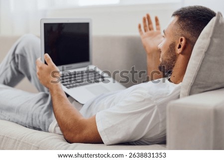 Engaged man communicating online while lounging at home, wearing casual attire and relaxed expression, enjoying a video call in a cozy setting.