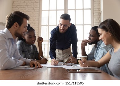 Engaged motivated young arabic male team leader leaning over table, discussing project ideas with involved mixed race partners team, drawing graphs on paper, explaining personal opinion at office. - Shutterstock ID 1517113595