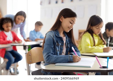 Engaged school children sit at desks, writing in their copybooks, creating studious atmosphere in classroom interior - Powered by Shutterstock