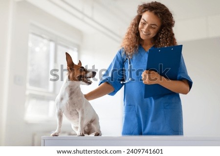 Engaged small dog with pricked ears interacting with happy female veterinarian holding clipboard in a well-lit veterinary clinic room