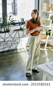 Engaged in a task, the young non binary individual stands in a vibrant office filled with greenery.