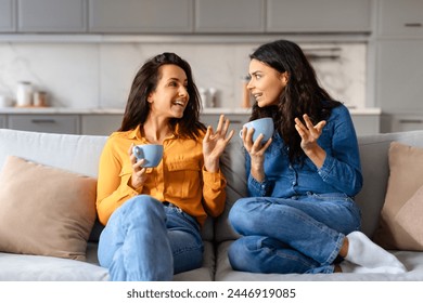 Engaged in a warm conversation, two young pretty women share stories over coffee on a beige couch at home - Powered by Shutterstock