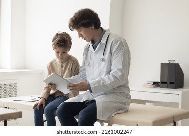 Engaged young pediatrician man showing content on tablet to patient kid, explaining examination result, diagnosis. Male doctor giving device to boy for playing, reading ebook. - Powered by Shutterstock