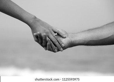 Engagement Couple Holding Hands With A Beach Background. A Couple Hold Hands With A Wedding Ring And Laguna Beach California Background. 