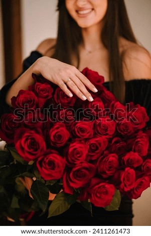 Engagement ring. Marriage proposal. Elegant floral template for design for Valentine's Day. A girl's hand with a wedding ring on a big bouquet of red roses. Love concept. Closeup. Side view.
