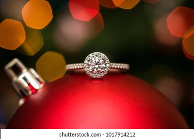 Engagement Ring On A Christmas Ornament With Lights In The Background.