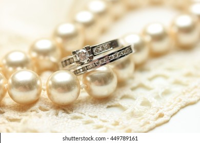 Engagement ring and wedding band with diamonds on a pearl necklace - Powered by Shutterstock