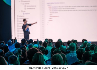 Engaging conference with speaker presenting programming concepts to audience. Large screen displaying code.