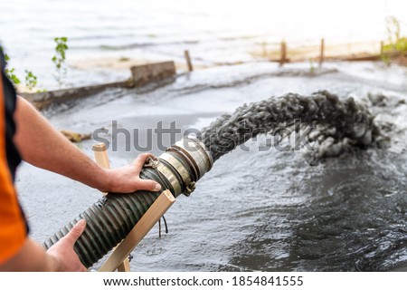 Engeneer hold pipe of power pump machine pouring mud sludge waste water with sand silt on ground. Sand-wash and coast-depeening. Septic sewage maintenance service. Industrial environment pollution