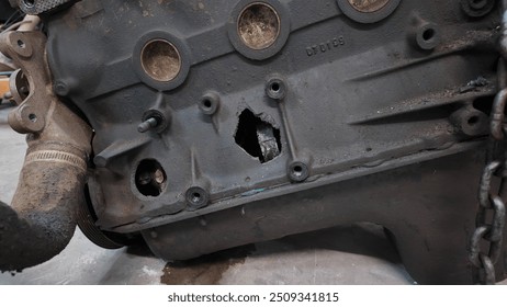Engine block sitting on the ground after being pulled out of the vehicle damaged after a rod and piston blew holes in the side after mechanical failure
