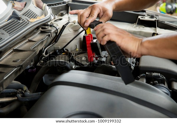 Engine engineer is replacing\
car battery because car battery is depleted. concept car\
maintenance.Selective focus charging car with electricity trough\
cables