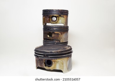 Engine Piston In Black Sludge And Burnt Oil, With Removed Oil Control Ring, Closeup. Pile Of Pistons On Background, Are Out Of Focus