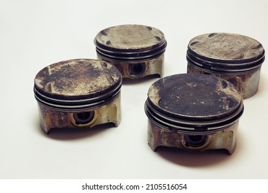 Engine Pistons Set Of Four. Worn Out Change Part Of Old Car Motor. Surfaces In Burnt Oil And Black Sludge. On White Background