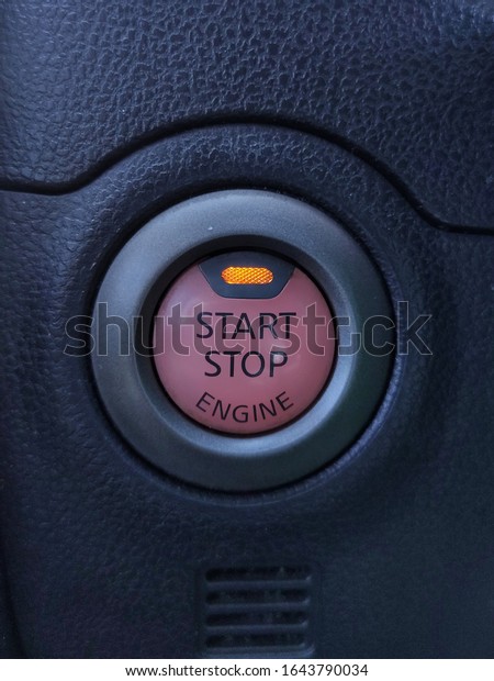 The engine start button stops with an\
orange light on the black car console\
background