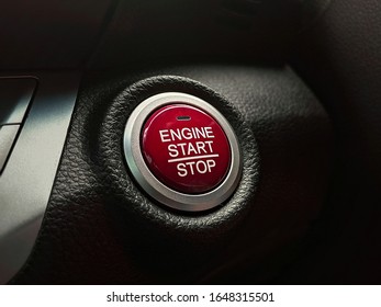 Engine start / stop button switch that has a red colour on a car console panel in a luxury car.