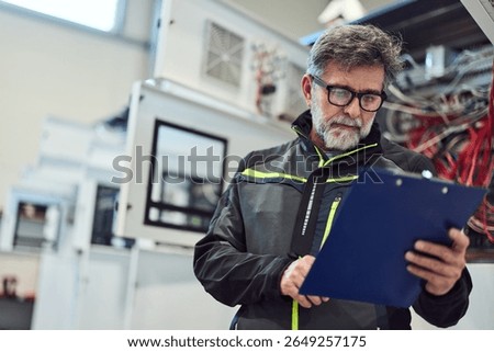 Engineer analyzing data on a clipboard inside a modern factory environment.