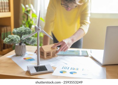 Engineer analyzing data on a digital tablet, assessing the performance of a miniature wind turbine and solar panel powering a model house, highlighting renewable energy solutions - Powered by Shutterstock - Get 15% off with code: PIKWIZARD15