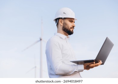 Engineer analyzing wind turbine data on a laptop, contributing to sustainable energy production in an outdoor setting under a blue sky