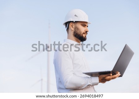 Engineer analyzing wind turbine data on a laptop, contributing to sustainable energy production in an outdoor setting under a blue sky