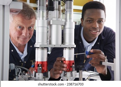 Engineer And Apprentice Working On Machine In Factory