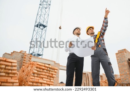 engineer architect with hard hat and safety vest working together in team on major construction site.