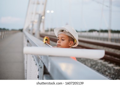 An engineer boy with a protective helmet on his head, looking at the plans on the bridge