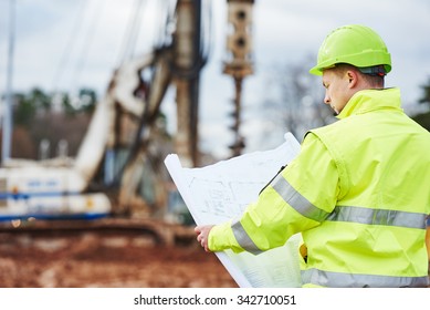 Engineer Builder With Blueprint Plan At Construction Site