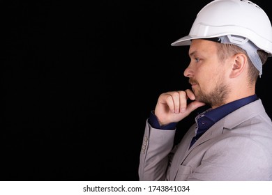 Engineer, builder, businessman in a white helmet on a dark background. Portrait. The concept of engineering, business, construction, urban life and the future.