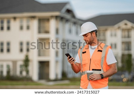 Engineer builder drinking take away coffee using phone on break. Builder at construction site. Buider with helmet on construction outdoor. Worker at construction site. Bilder in hardhat.