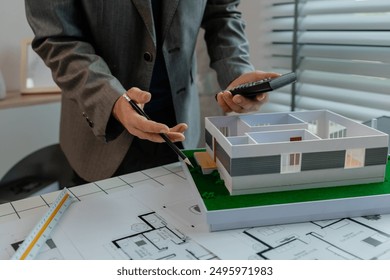An engineer is calculating whether the structural proportions of a house model are correct with a calculator, an architect is using calculator to check numbers from a blueprint