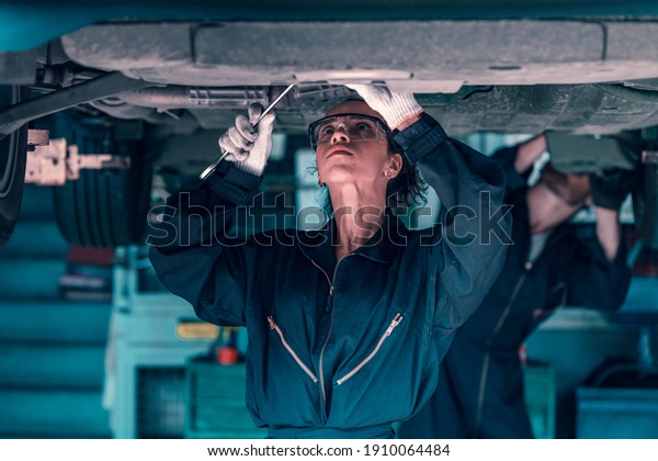 Engineer car mechanic under checking under the car by\
see detail with screwdriver on hand for maintenance and fixed\
it.